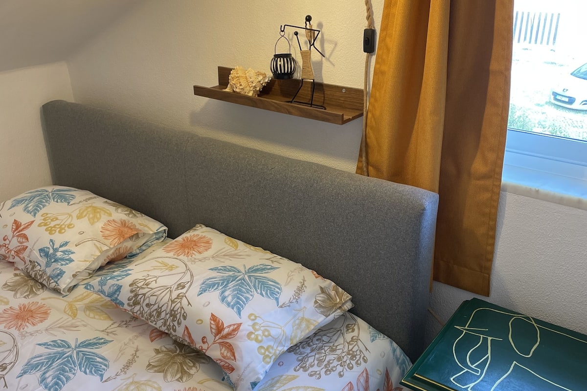 A bedroom with a bed, a bedside table, a lamp, and a window with curtains.