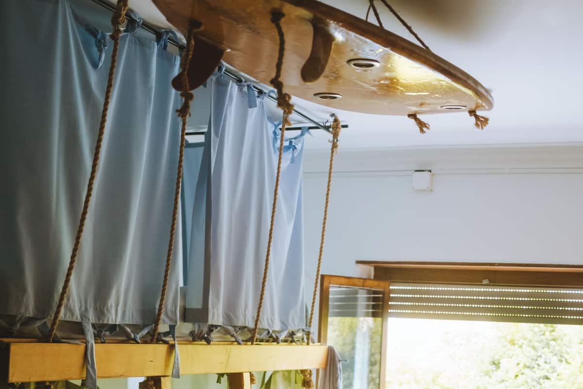 A bunk bed with a ladder, a wooden ceiling fan, and a window with blinds.