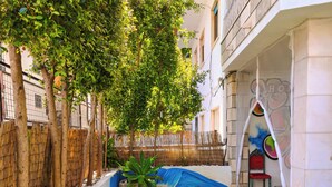 A courtyard with a grassy path, trees, a bamboo fence, and a building with a balcony. - Lisbon Soul Surf Camp (Cascais)