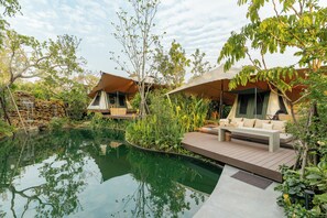 A modern outdoor pool area with a wooden deck and lounge seating, surrounded by lush greenery and a clear pool reflecting the sky. - CAMP CAYLA - EDEN (Chiang Mai)