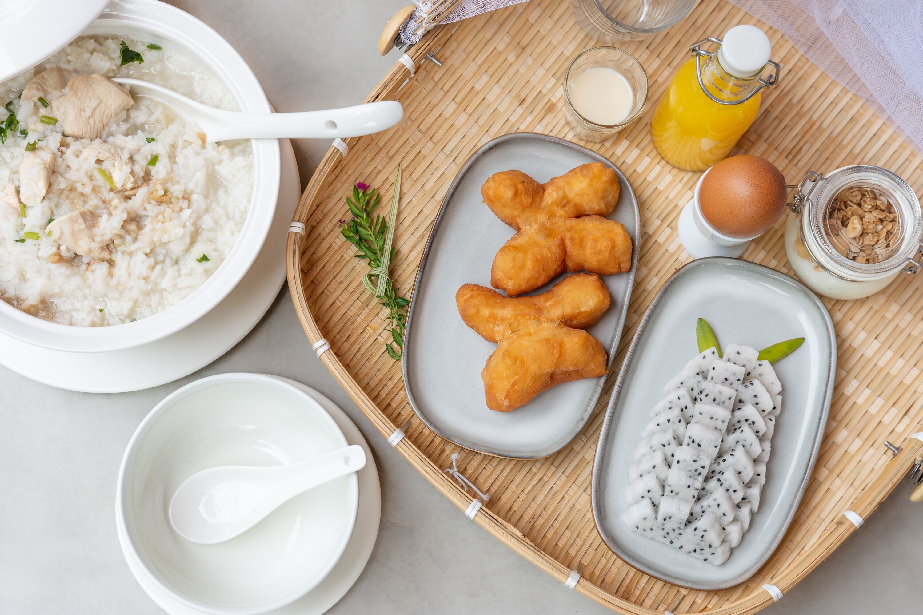 Bandeja de desayuno con un tazón de arroz, tres porciones de pan frito, un plato de pitahaya en rodajas, un vaso de jugo de naranja, una botella de leche y un tarro de granola.