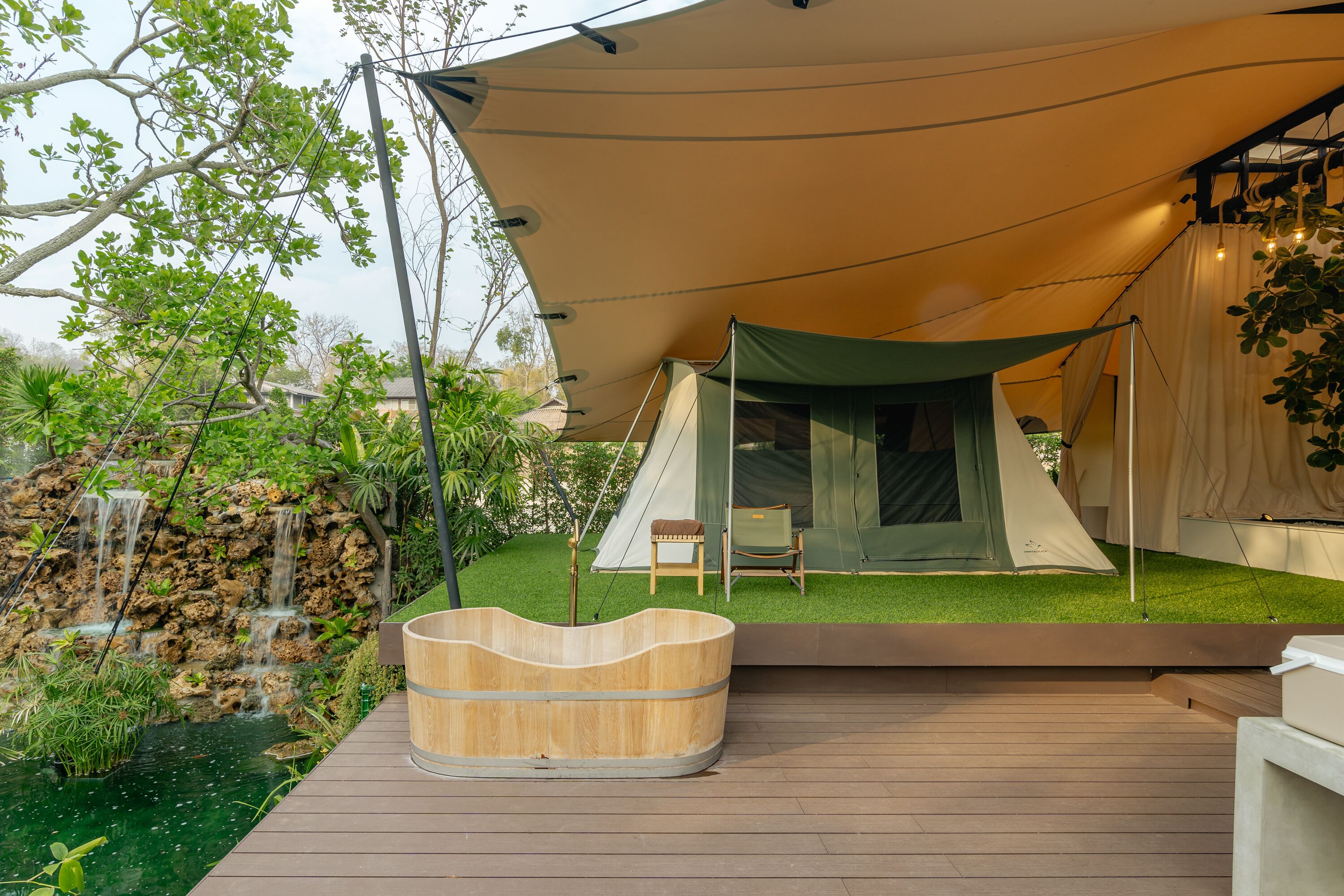A tented outdoor area with a wooden hot tub, a small table, and a chair.