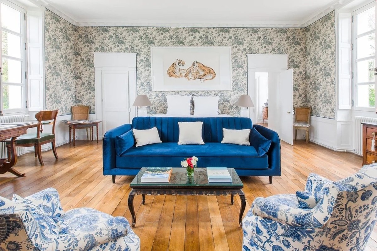 A room with a blue sofa, floral wallpaper, and a framed picture above the sofa.