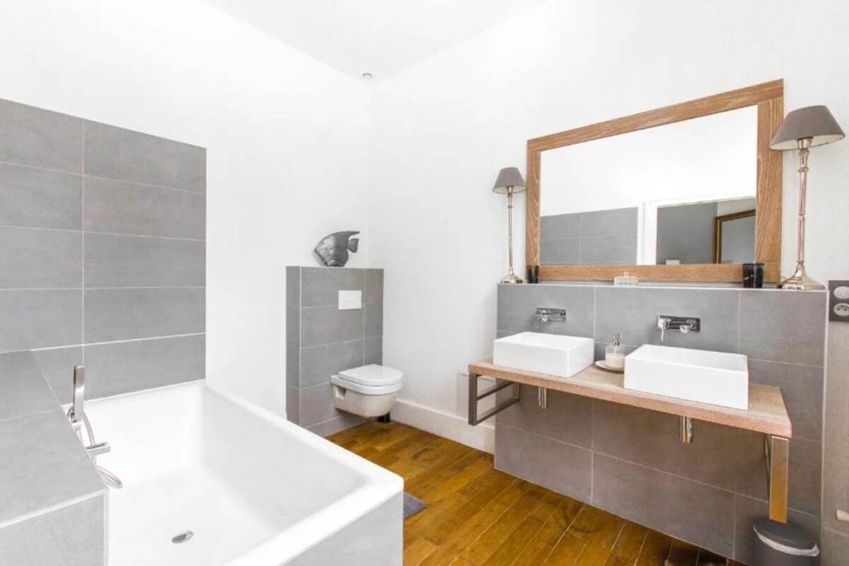 A modern bathroom with a large bathtub, two sinks, and a toilet.