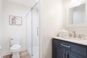 A modern bathroom with a glass shower enclosure, a toilet, a sink with a mirror, and a framed picture on the wall.