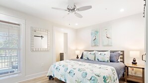 A bedroom with a bed, nightstands, a ceiling fan, artwork, and a window with blinds. - Amazing Heron Loft in Gulf Shores entertainment district (Gulf Shores)