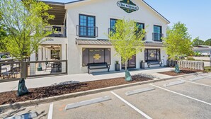 A two-story building with a sign reading "The Galway." It features a balcony on the second floor, a parking lot in front, and a small garden area with trees. - Amazing Heron Loft in Gulf Shores entertainment district (Gulf Shores)