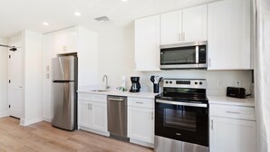 A modern kitchen with stainless steel appliances, white cabinetry, and a wooden floor. - Amazing Heron Loft in Gulf Shores entertainment district (Gulf Shores)