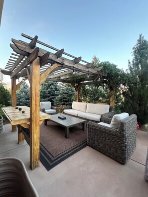 An outdoor patio area with a wooden pergola, a sofa, a table, and a coffee table. - Immaculate 5-Bedroom Aurora Retreat — Luxury, Comfort & Colorado Adventure (Aurora)