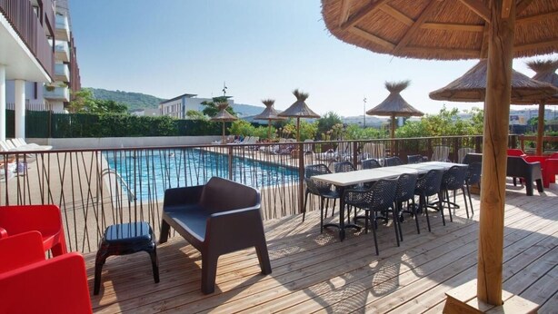 Ein Poolbereich auf dem Dach mit Holzterrasse, Liegestühlen und Sonnenschirmen.