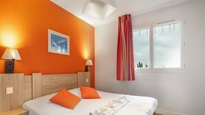 Ein Hotelzimmer mit Bett, zwei Kissen, einem Nachttisch, einer Lampe, einem Fenster mit Vorhängen und einem Bild an der Wand.