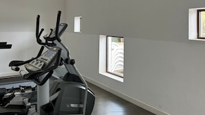 Ein Fitnessraum mit einem Ergometer, einem Laufband und einer Wand mit kleinen Fenstern.