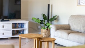 Ein Wohnzimmer mit einer Couch, einem Couchtisch, einer TV-Konsole mit Büchern und einer Pflanze.