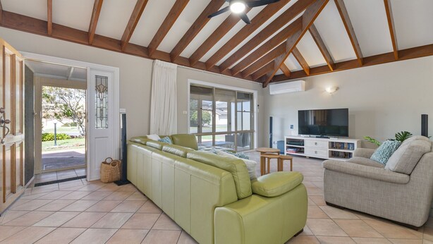 Ein geräumiges Wohnzimmer mit einem grünen Sofa, einem grauen Sofa und einem Flachbildfernseher. Eine Glastür öffnet sich zu einer Terrasse.