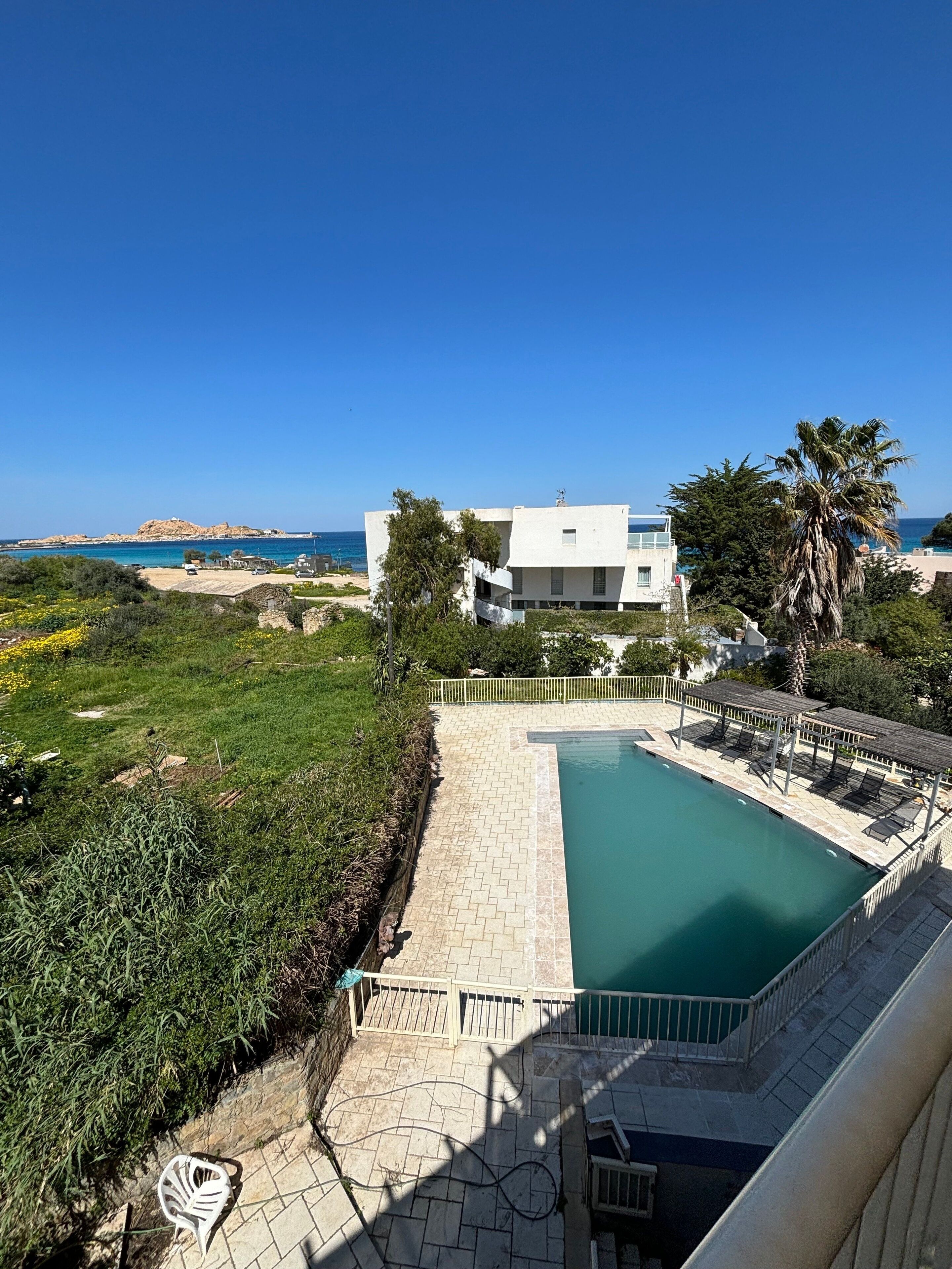 Un espace piscine moderne offrant une vue dégagée sur la mer, avec un bâtiment en arrière-plan.