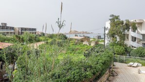 A residential area with a paved patio, a white building with balconies, and a view of a body of water in the background. - Le Petra Paoli - Front de mer -  Appt climatisé avec piscine (L'Île-Rousse)