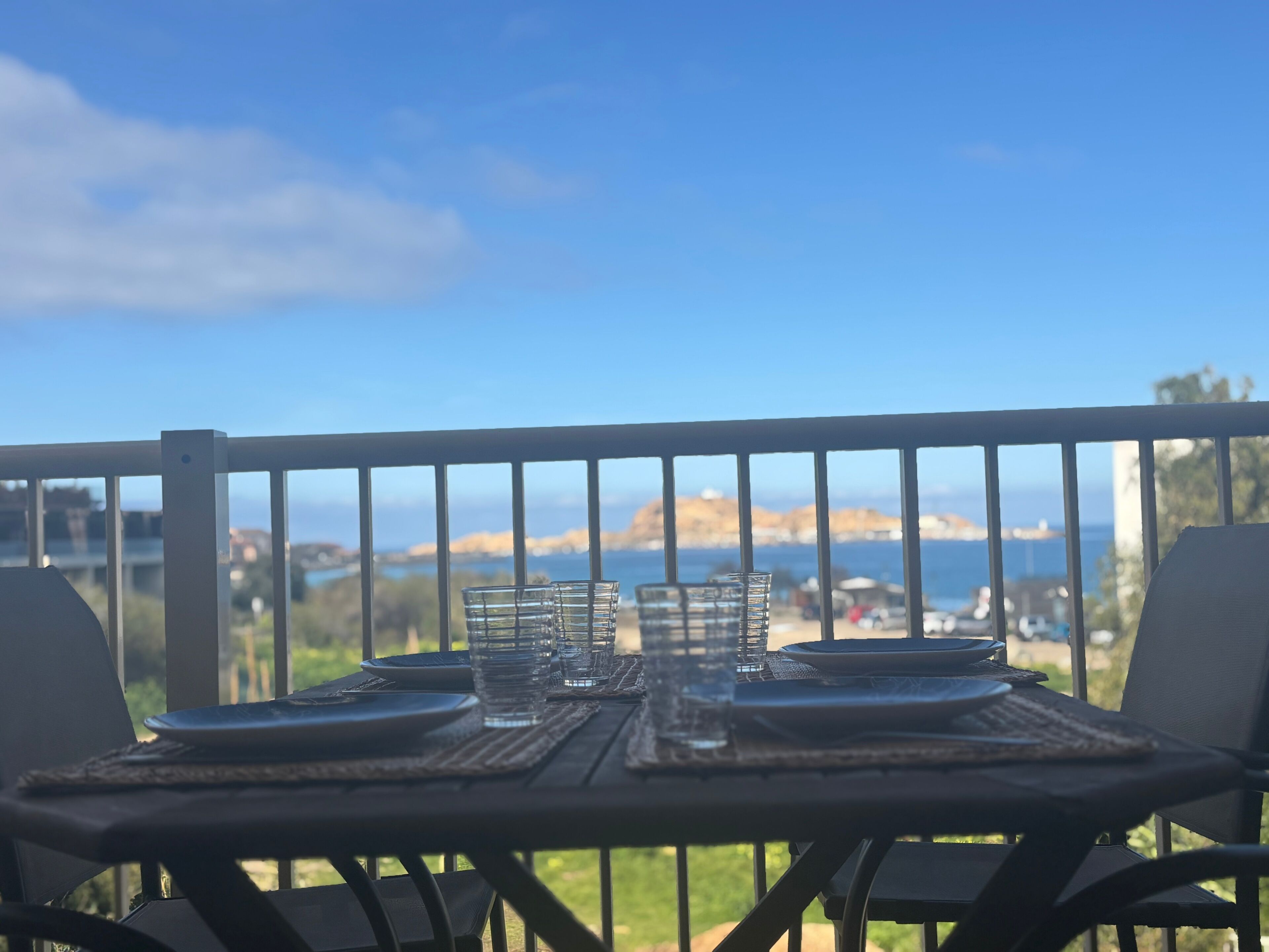 A table set for two with glasses and plates, overlooking a scenic view of hills and water.