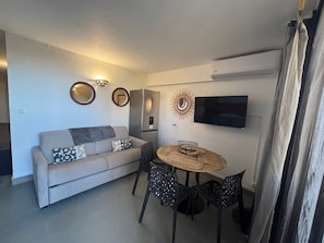 Um espaço compacto com sofá, mesa de jantar e cadeiras. Uma televisão de tela plana está fixada na parede.