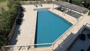 A rectangular swimming pool with a tiled deck, surrounded by a white fence, and shaded by a pergola. - L'Isula - Front de mer -  Appt pour 5 climatisé avec piscine (L'Île-Rousse)