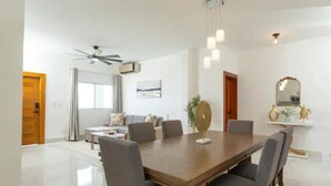 A modern dining area with a wooden table, grey upholstered chairs, a ceiling fan, and a chandelier.