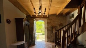 A hallway with a wooden staircase, a chandelier, and a view of greenery outside.