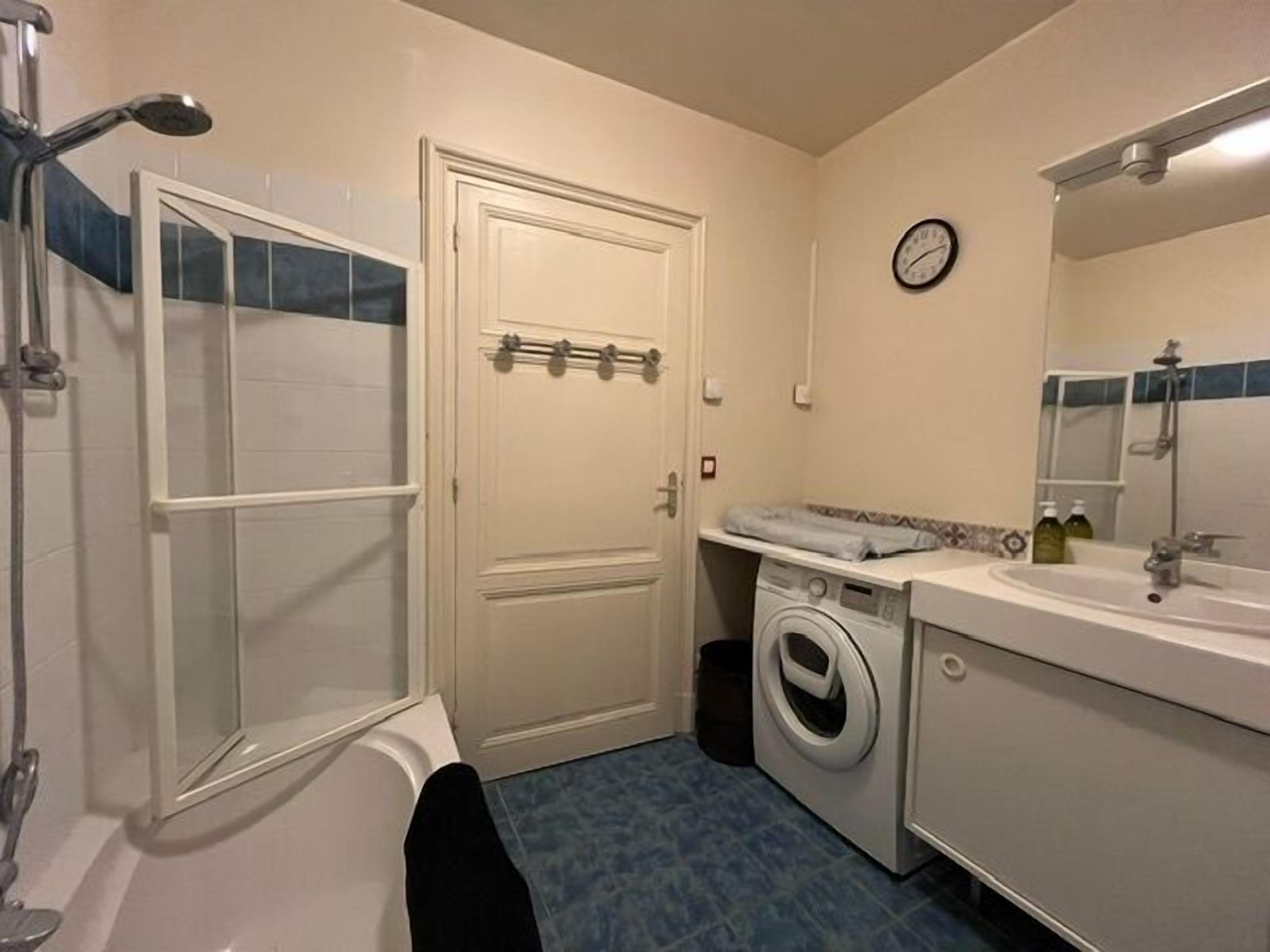 Une petite salle de bain comprenant une baignoire, un lave-linge, un lavabo et un miroir.