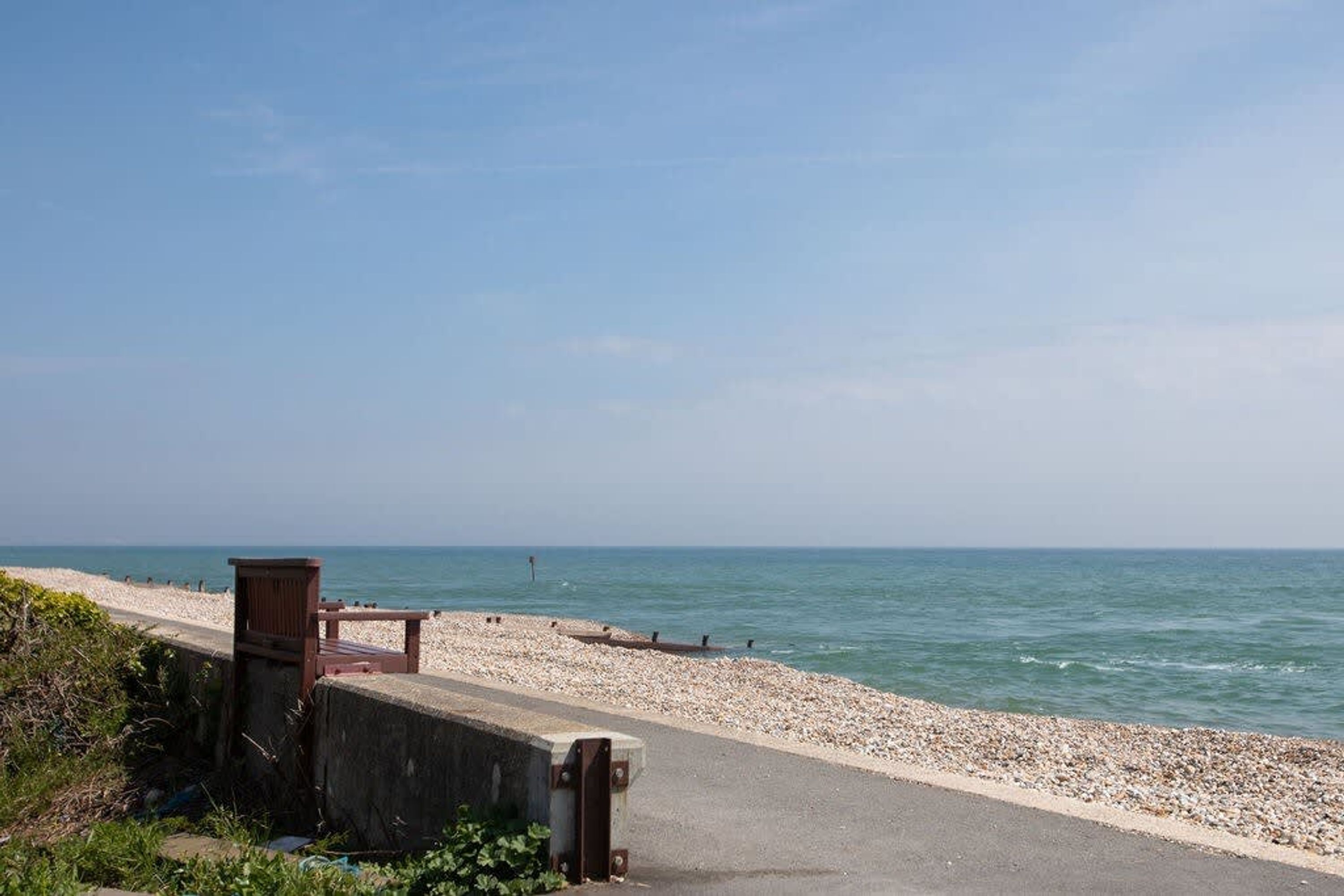 Une plage de galets avec une promenade en béton et un banc en bois.
