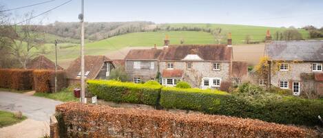 A rural setting with stone houses, a hedge, and a clear view of the countryside.