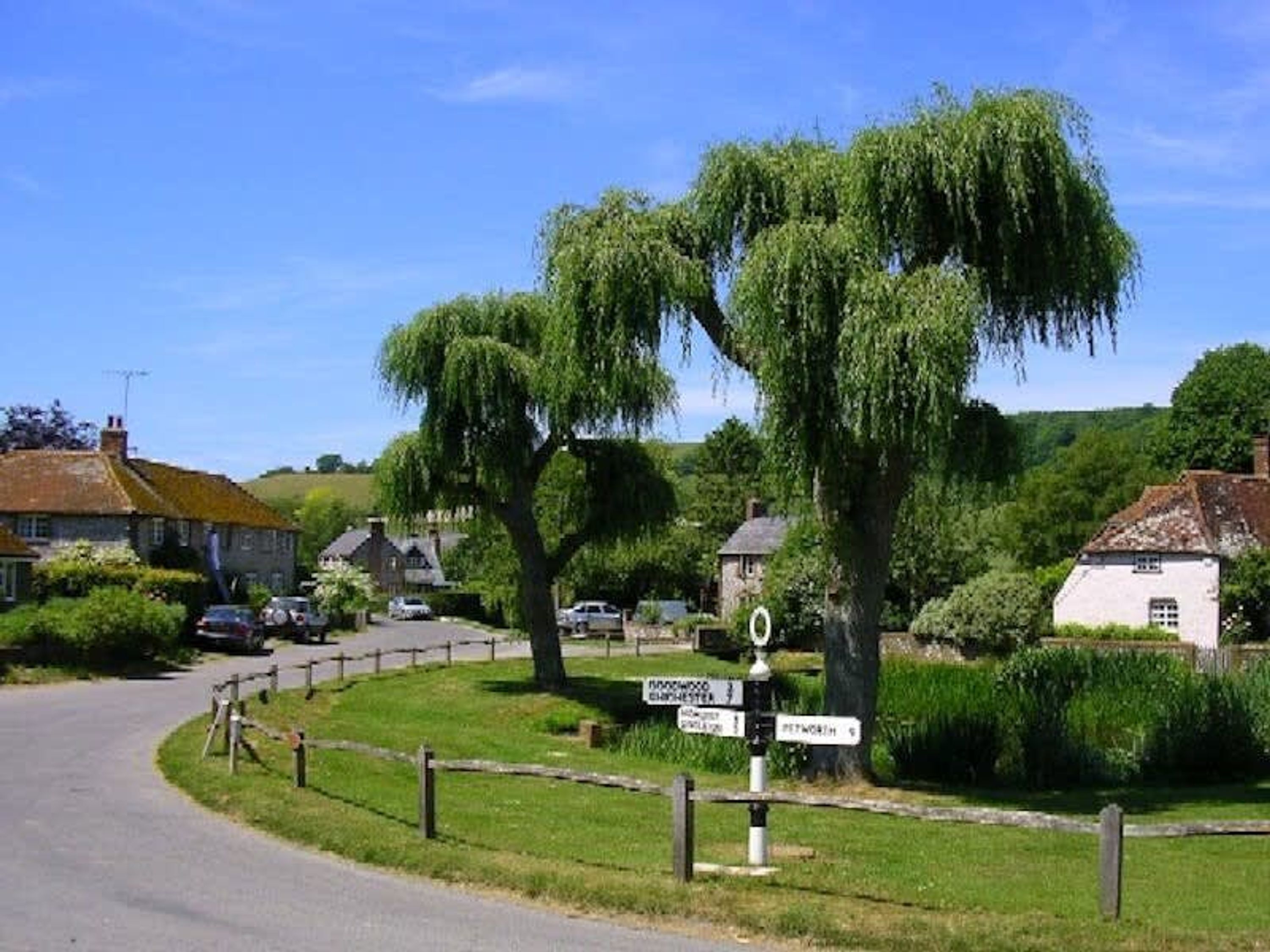 A rural road with a directional signpost, houses, and lush greenery.