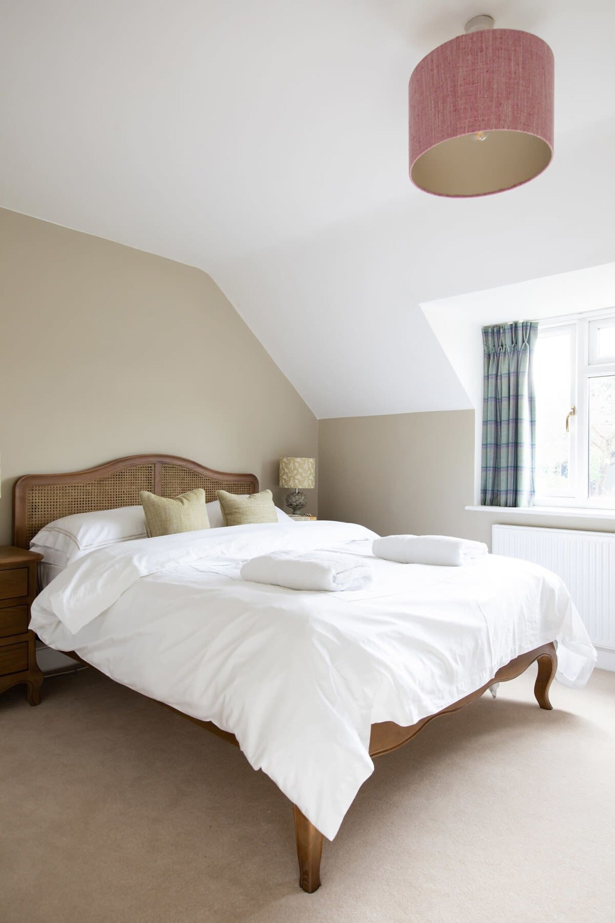 A bedroom with a wooden bed, white bedding, a bedside lamp, and a window with curtains.