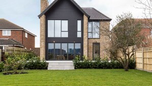A modern two-story house with a dark facade, large windows, and a well-maintained lawn.