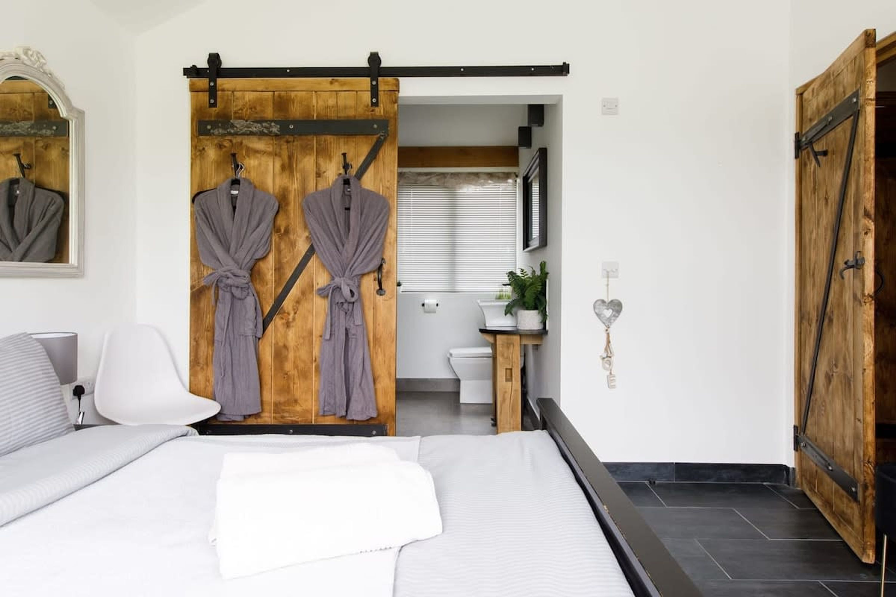 A bedroom with a bed, a sliding door, a white chair, and a small bathroom visible through the door.