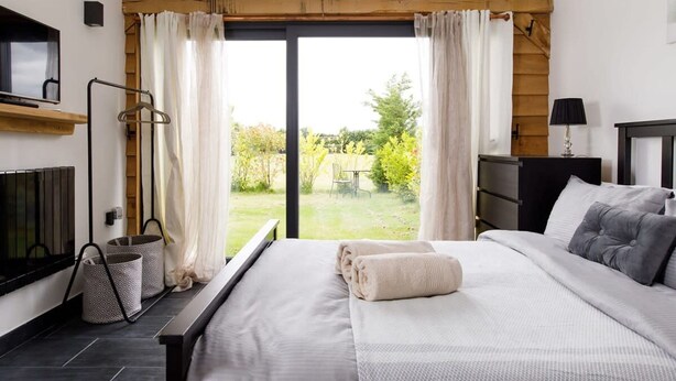 A bedroom with a bed, a TV, a bedside table, a lamp, and a view of the garden.