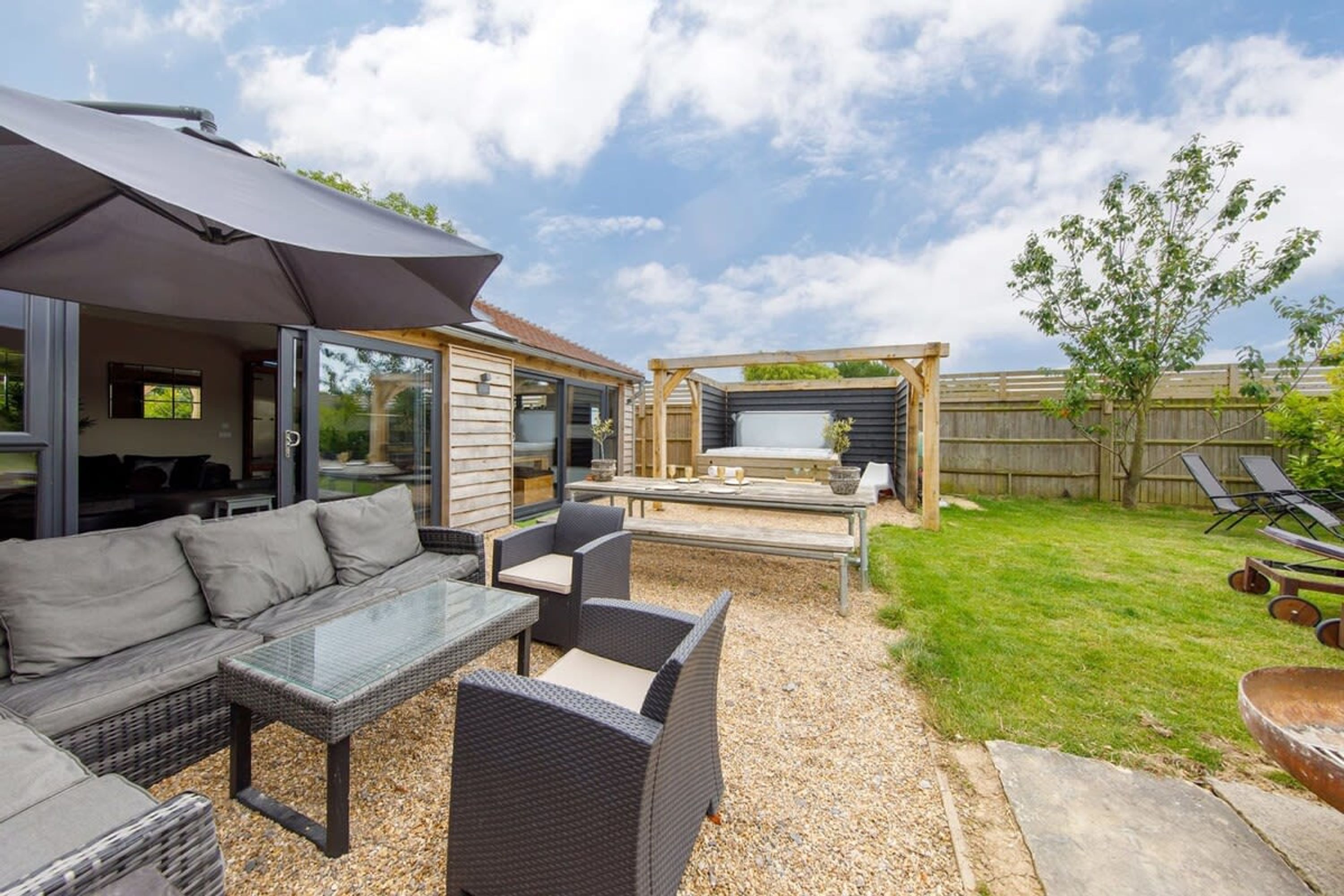 An outdoor patio area with wicker furniture, a glass table, and a pergola.