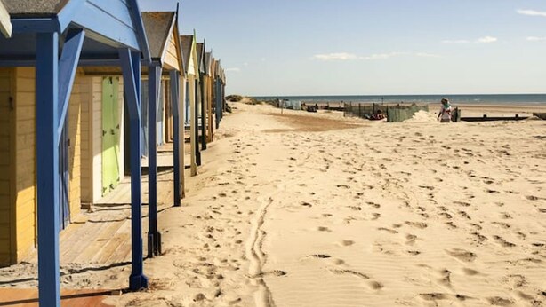 A row of beach huts with a sandy beach and ocean in the background.