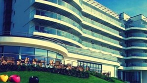 A modern multi-story hotel with a curved facade, large windows, and outdoor seating areas.