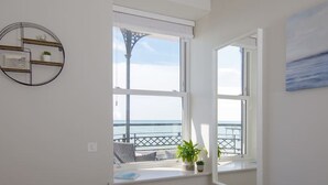 A bedroom with a large window overlooking a balcony with a view of the sea. There is a bed with white linens and a circular wall decoration.