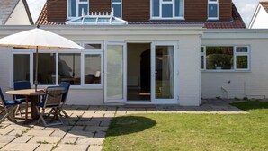 Ein zweistöckiges Haus mit einer Terrassenanlage, die einen Tisch und Stühle, eine Glastür und einen kleinen Garten umfasst.