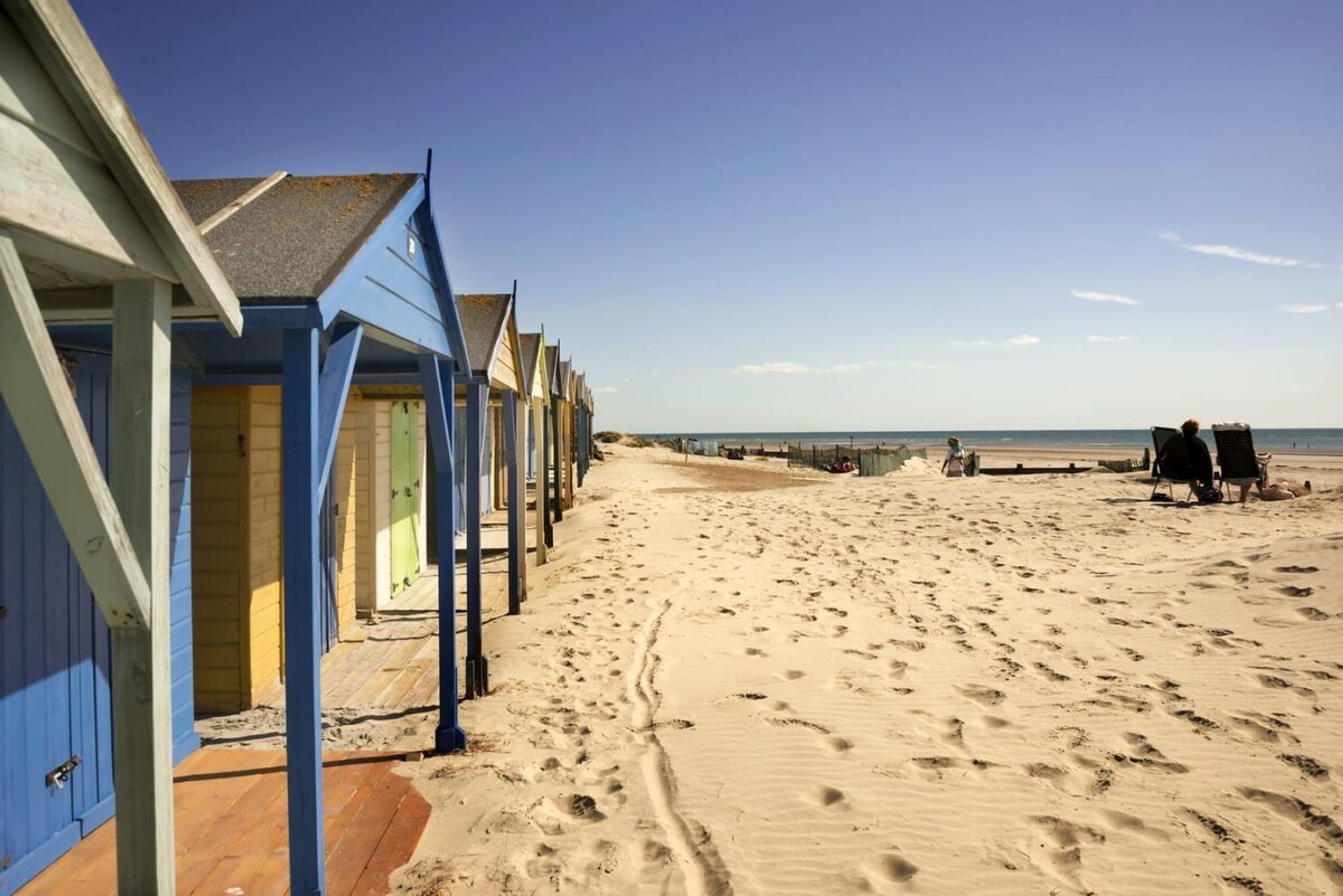 Una hilera de cabañas de playa con una playa de arena al fondo.