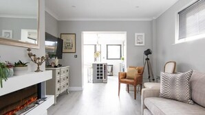 A modern living room with a fireplace, a sofa, a television, and a dining area in the background. - Seaside Serenity 3-bed Deck Garden Near Shore (Chichester)