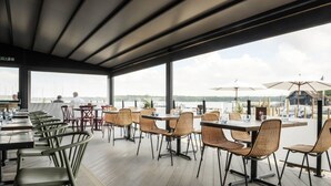 An outdoor dining area with tables and chairs, large windows, and umbrellas. - Seaside Serenity 3-bed Deck Garden Near Shore (Chichester)