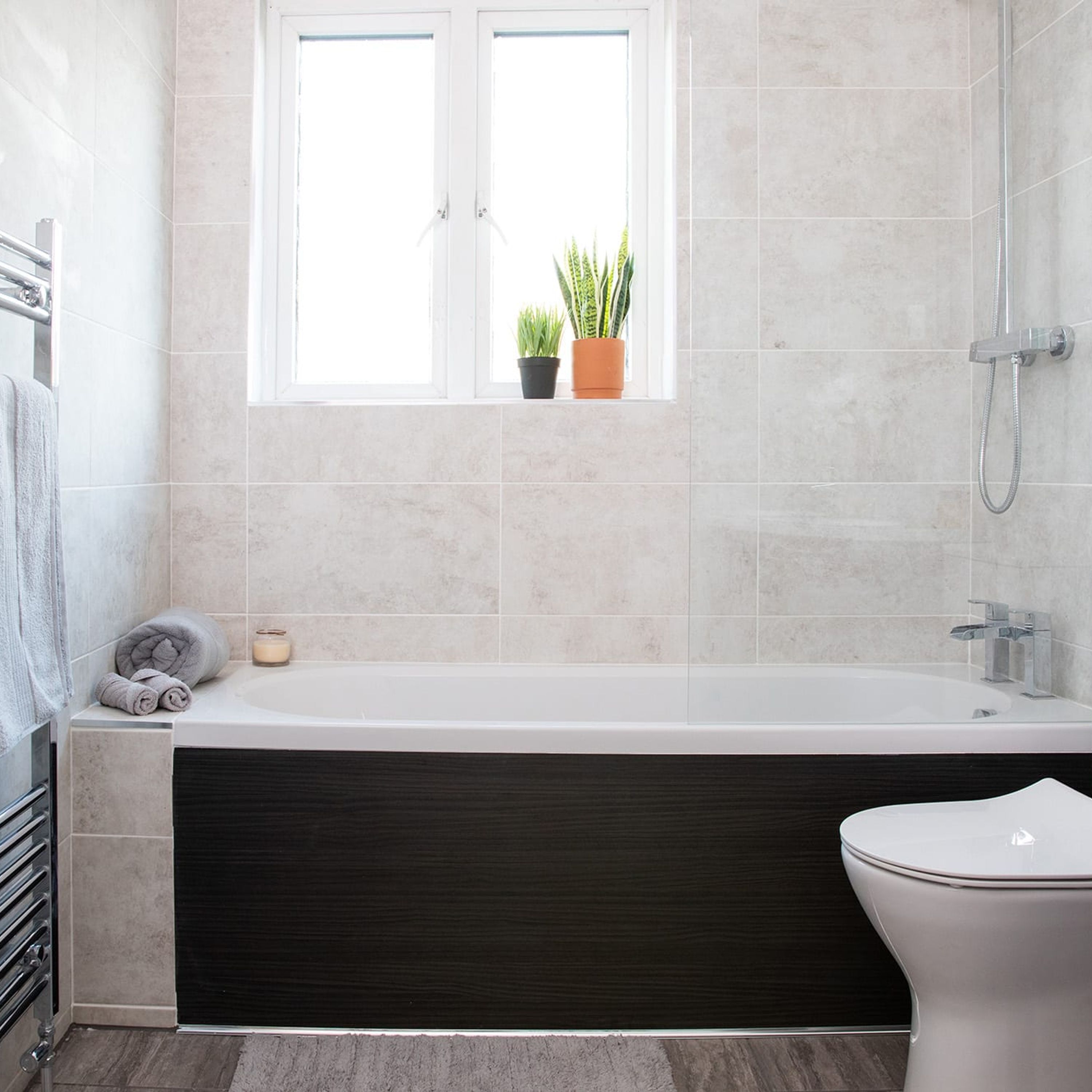 Een moderne badkamer met een badkuip, toilet en een raam met planten.
