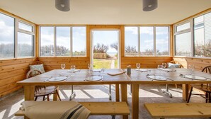 Une table à manger en bois, avec des chaises et un banc, pouvant accueillir quatre personnes, et offrant une vue sur l’extérieur grâce à de grandes fenêtres.