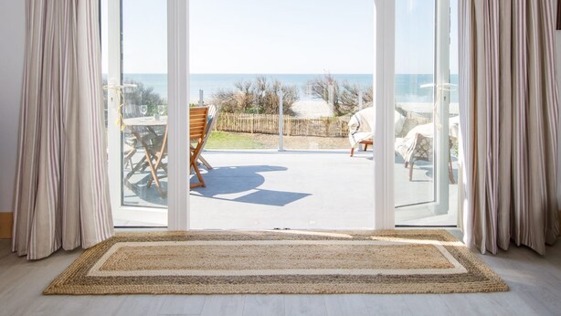 Une pièce spacieuse dotée d’une grande porte-fenêtre coulissante qui donne sur une terrasse extérieure offrant une vue sur la mer.