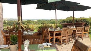 An outdoor dining area with wooden tables and chairs, green umbrellas, and a scenic view of the countryside. - Countryside Annexe Near Goodwood (Chichester)