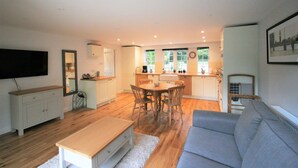 A modern living room with a grey sofa, wooden coffee table, and a dining area with a round table and chairs. - Countryside Annexe Near Goodwood (Chichester)