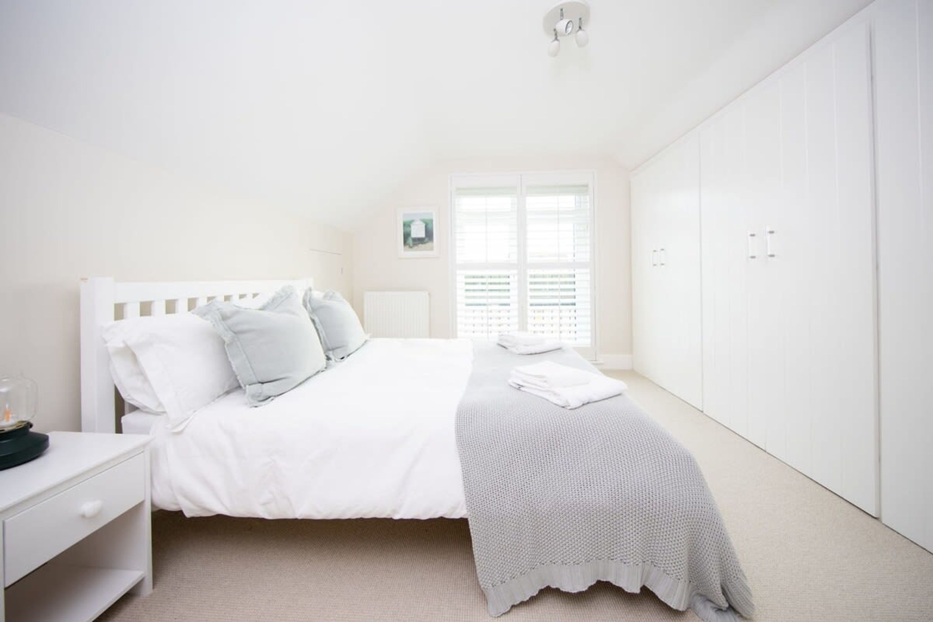 A bedroom with a bed, white wardrobe, and a window with blinds.