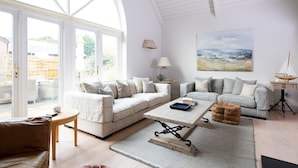 A spacious living room with two sofas, a coffee table, and a lamp. There is a large window providing a view of the outdoors. - Superior House for 6 Near Beach w Parking Garden (Chichester)