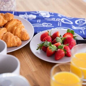 A breakfast setting with croissants, strawberries, and orange juice on a wooden table. - Stylish Cosy Annexe in Pretty Sailing Village (Chichester)