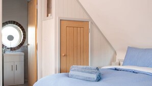 A bedroom with a bed, a wooden door, a bathroom with a sink, and a circular mirror. - Stylish Cosy Annexe in Pretty Sailing Village (Chichester)